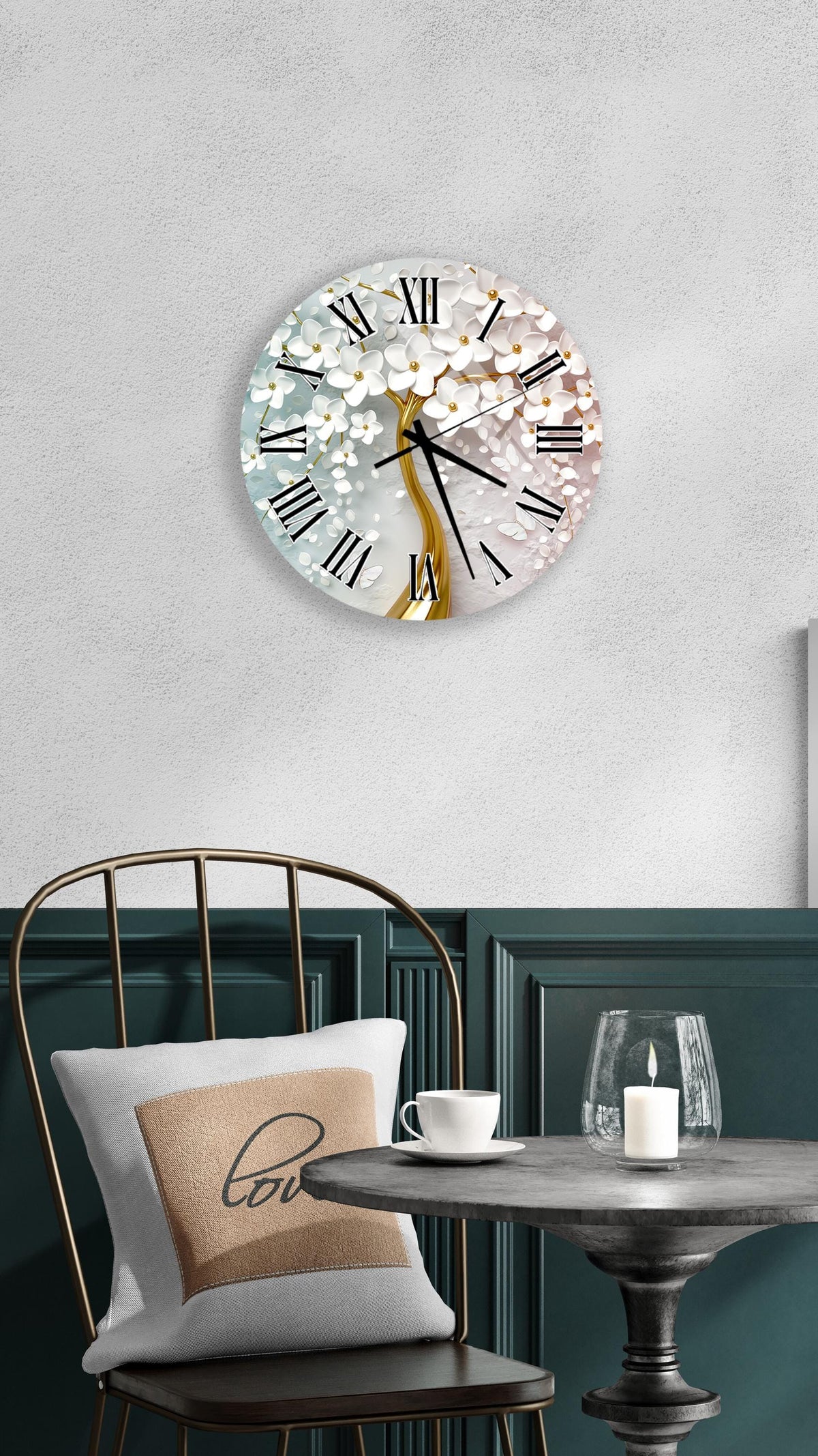 a wall clock with a white and gold design, mounted on a wall above a table with a white tablecloth. The table has a white candle and a white mug on it. A chair is positioned in front of the table, and there is a pillow with the word "love" on it.