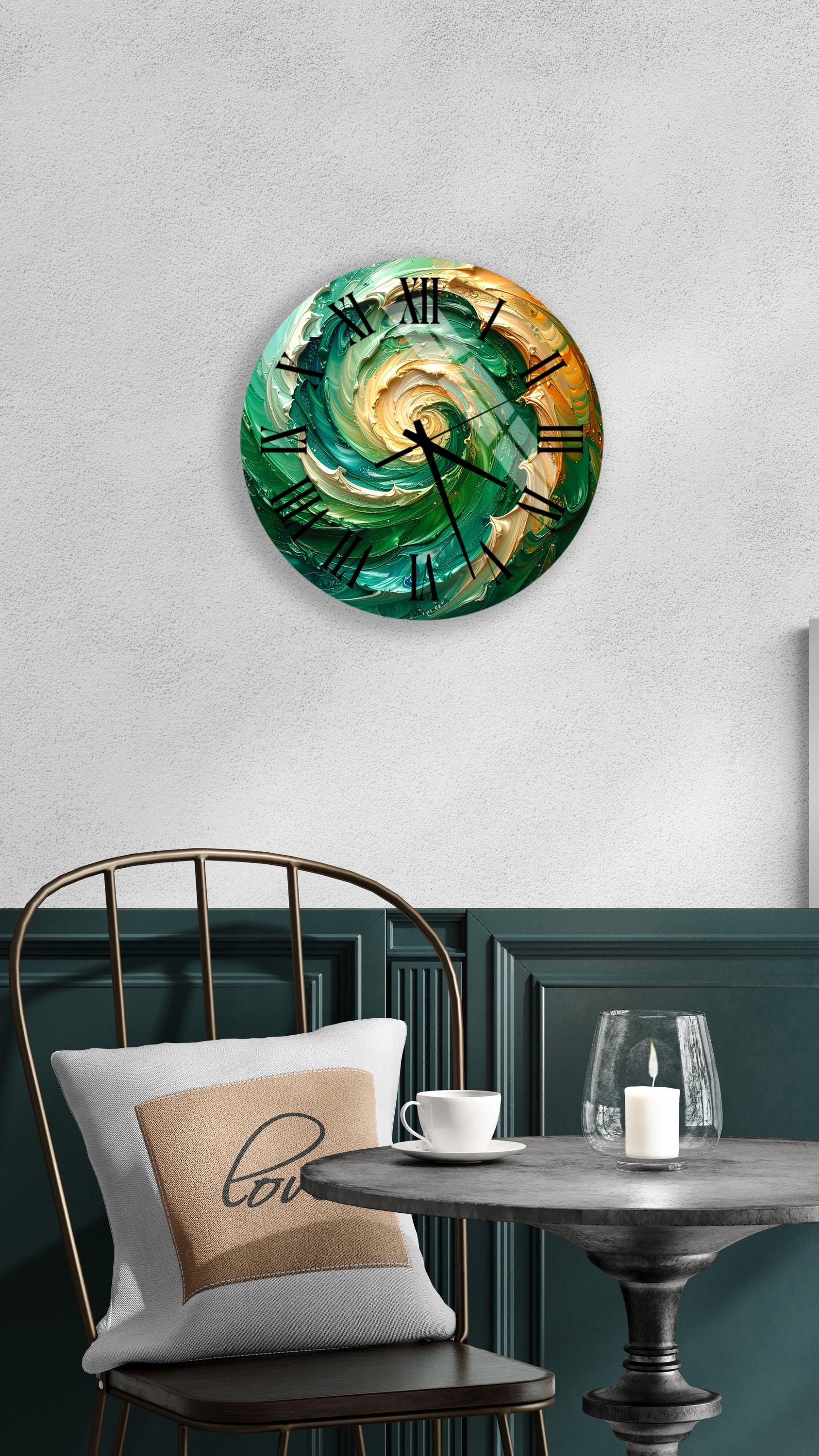 a round wall clock with a swirling green and orange design, mounted on a white wall above a black metal chair. The chair has a white pillow with the word "love" printed on it. In front of the chair, there is a small table with a glass candle holder and a white teacup.