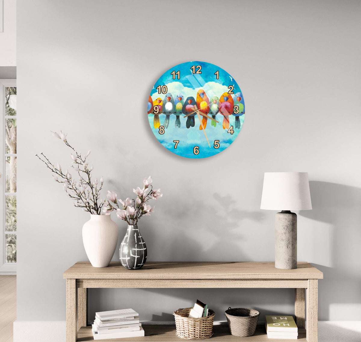 a clock with a bird design on a wall, a wooden table with a vase of flowers, a lamp, and some books.