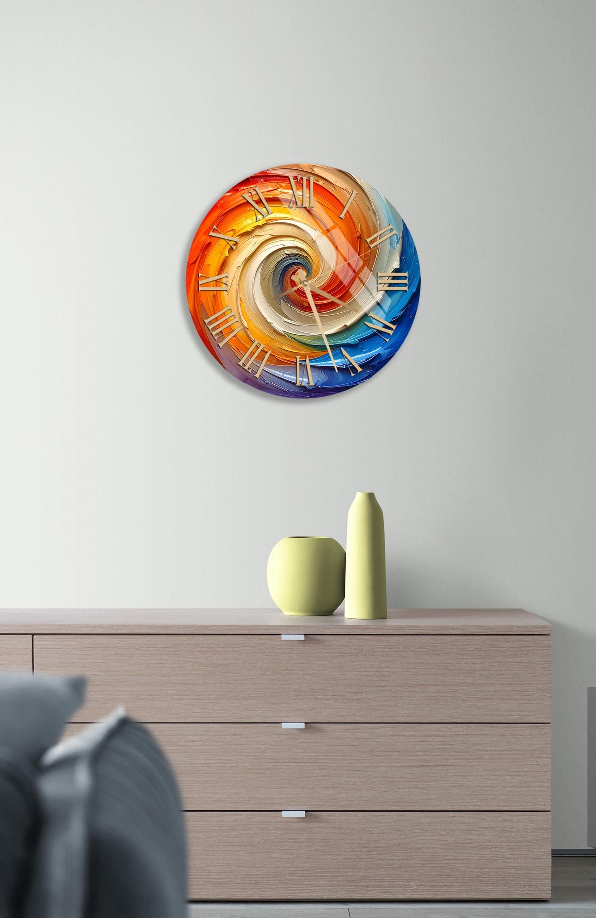 a modern clock with a spiral design on a white wall, mounted above a wooden dresser with a vase and a small sculpture on top.
