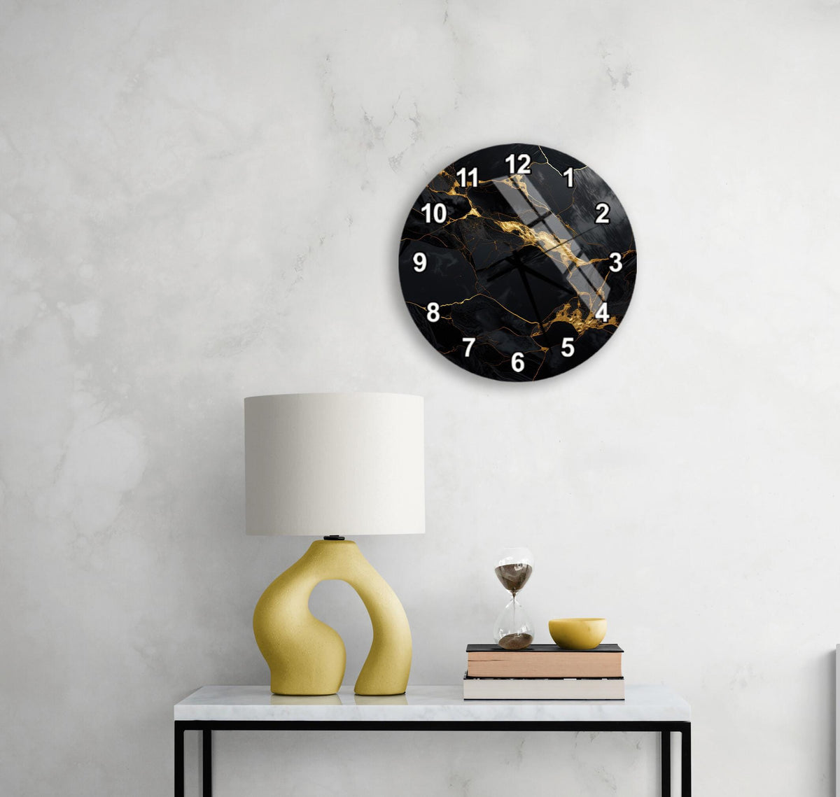 a modern black and gold wall clock with a white base, hanging on a white wall above a white table with a yellow lamp and a stack of books.