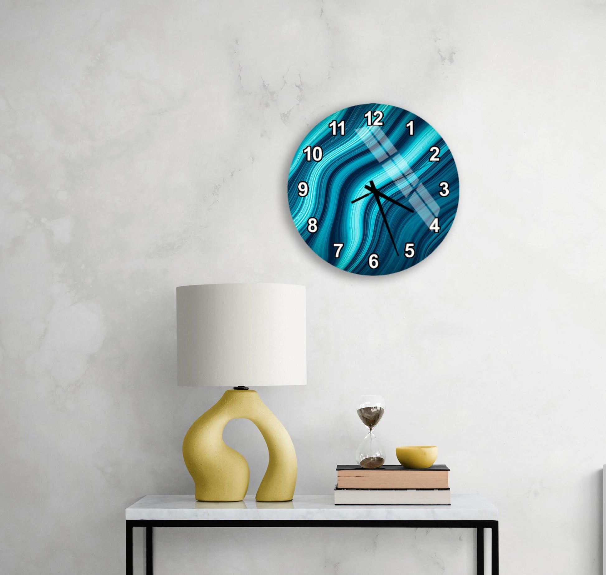 a modern living room with a white marble wall, a round clock with a blue and white abstract design, a yellow lamp with a unique curved base, and a small table with a book and a glass of water.