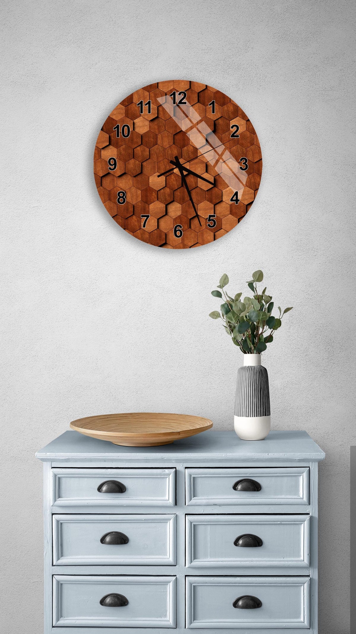 a wall clock with a wooden texture, a wooden tray, a vase with greenery, and a light blue dresser with six drawers.