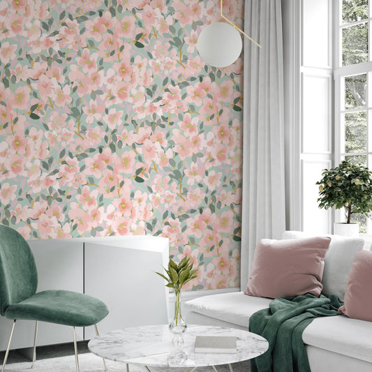 a living room with a floral wallpaper on the wall, a white sofa with pink pillows, a green armchair, and a round marble coffee table with a vase of flowers.