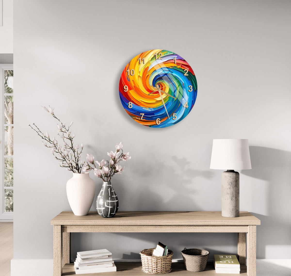 a wall clock with a colorful spiral design, a wooden table with a lamp, a vase with flowers, and some books on a shelf.