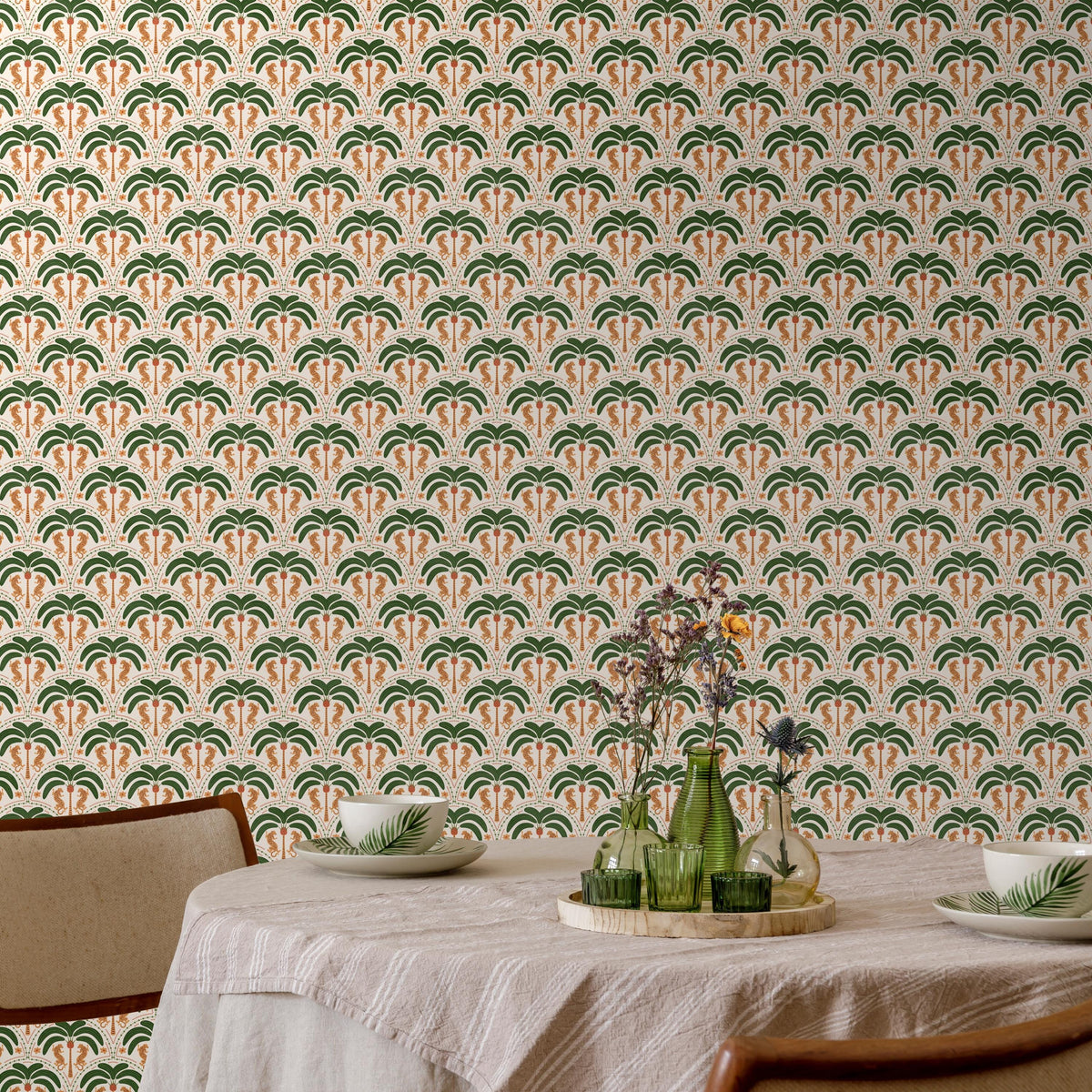 a dining table set with a white tablecloth, two white plates, and two green vases with flowers. The table is positioned against a wall with a repeating pattern of palm trees and leaves in shades of green and orange.