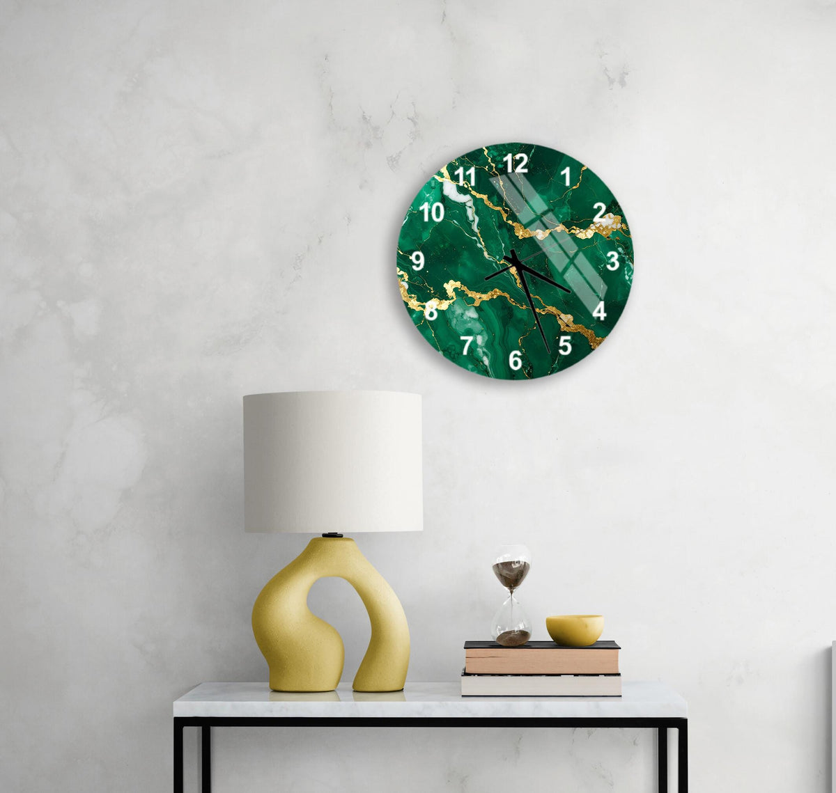 a modern living room with a green marble clock hanging on the wall above a white table. The table has a yellow lamp and a stack of books, creating a cozy and stylish atmosphere.