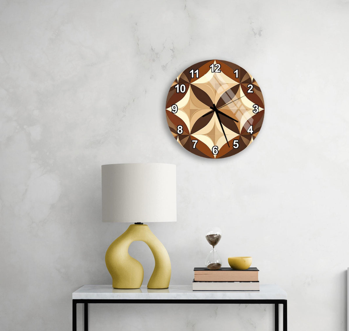 a modern wall clock with a brown and beige design, mounted on a white wall above a white table with a yellow lamp and a stack of books.