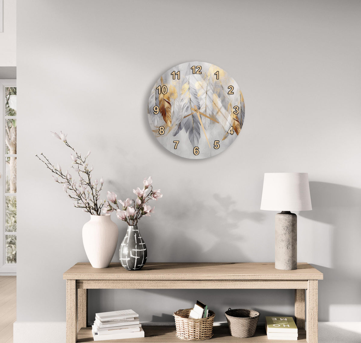 a modern living room with a wooden console table, a round wall clock with a feather design, a lamp, a vase with pink flowers, and a stack of books.