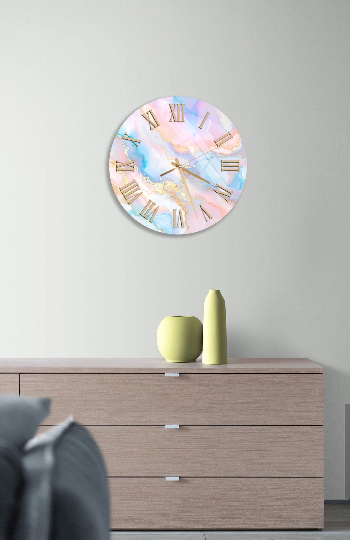 a wall clock with a marble-like design, mounted on a wall above a wooden dresser. The dresser has three drawers and contains a yellow vase and a small green pot.