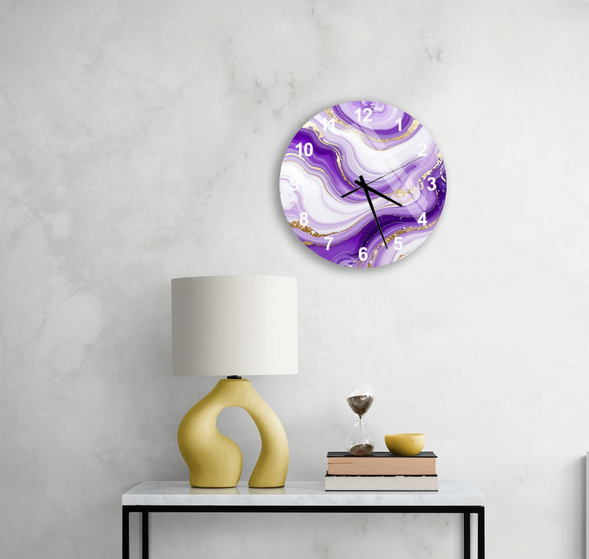 a white wall with a round clock displaying a purple marble design, a yellow lamp, a stack of books, and a glass of wine on a white table.