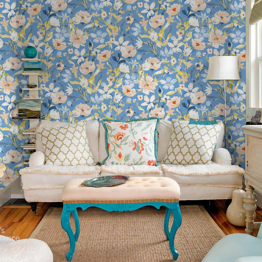 a cozy living room with a floral wallpaper, a white sofa with patterned throw pillows, a blue and white ottoman, and a wooden coffee table.
