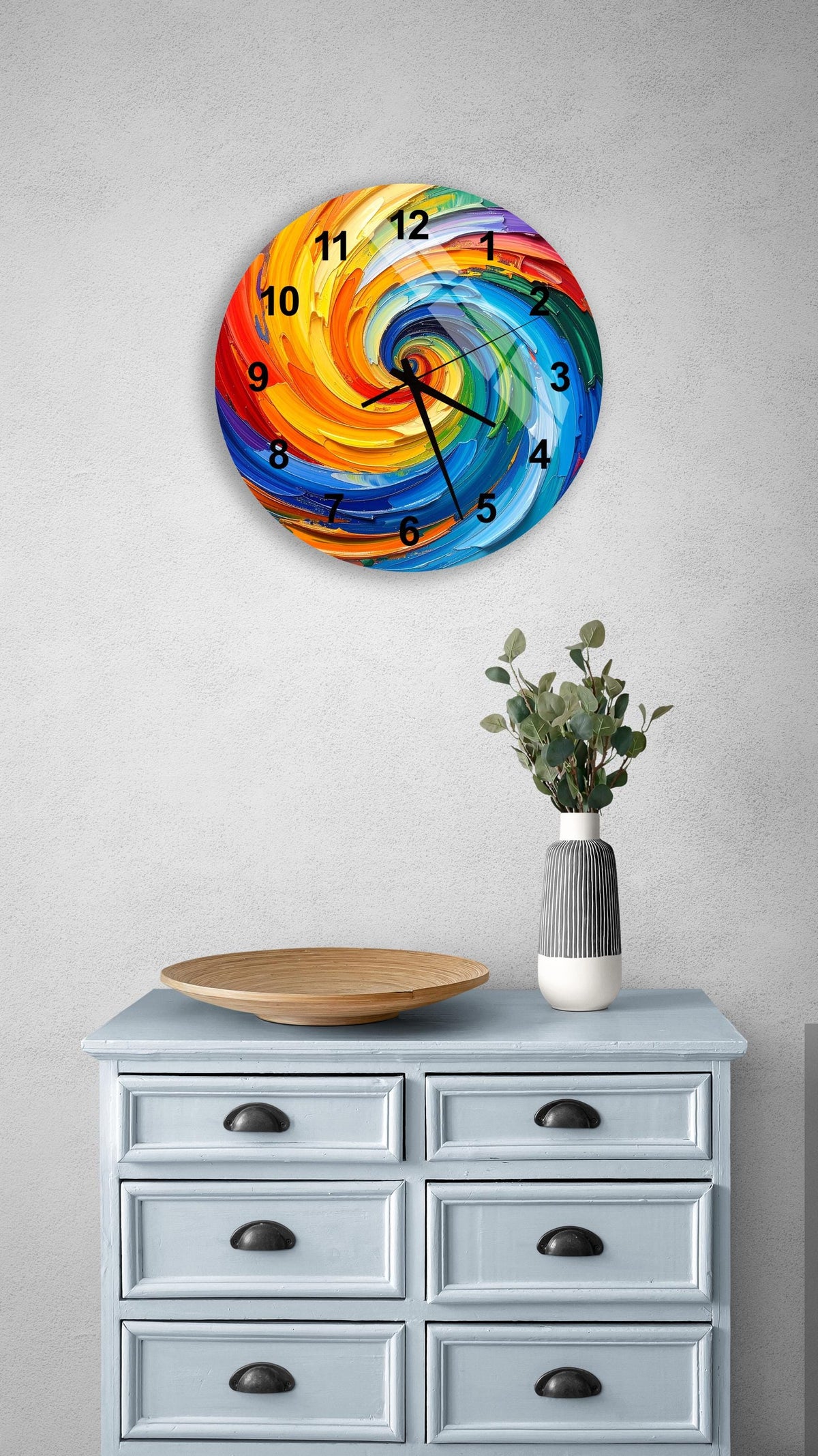 a colorful, abstract clock with swirling patterns on a wall above a light blue dresser with six drawers. The dresser also has a small plant and a wooden bowl on it.