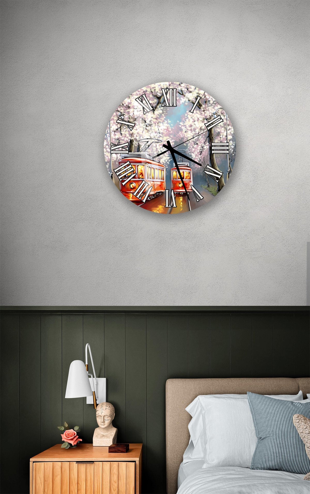 a wall clock with a design of a trolley car and cherry blossoms, mounted on a wall above a bedside table with a lamp and a small statue.