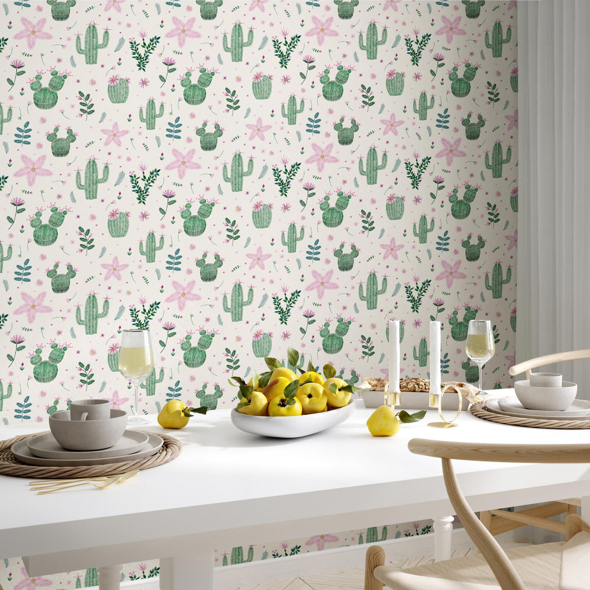 a dining table set with plates, bowls, and glasses, along with a bowl of fruit, including apples and pears. The table is set against a wall with a repeating pattern of cacti and flowers in shades of pink and green.