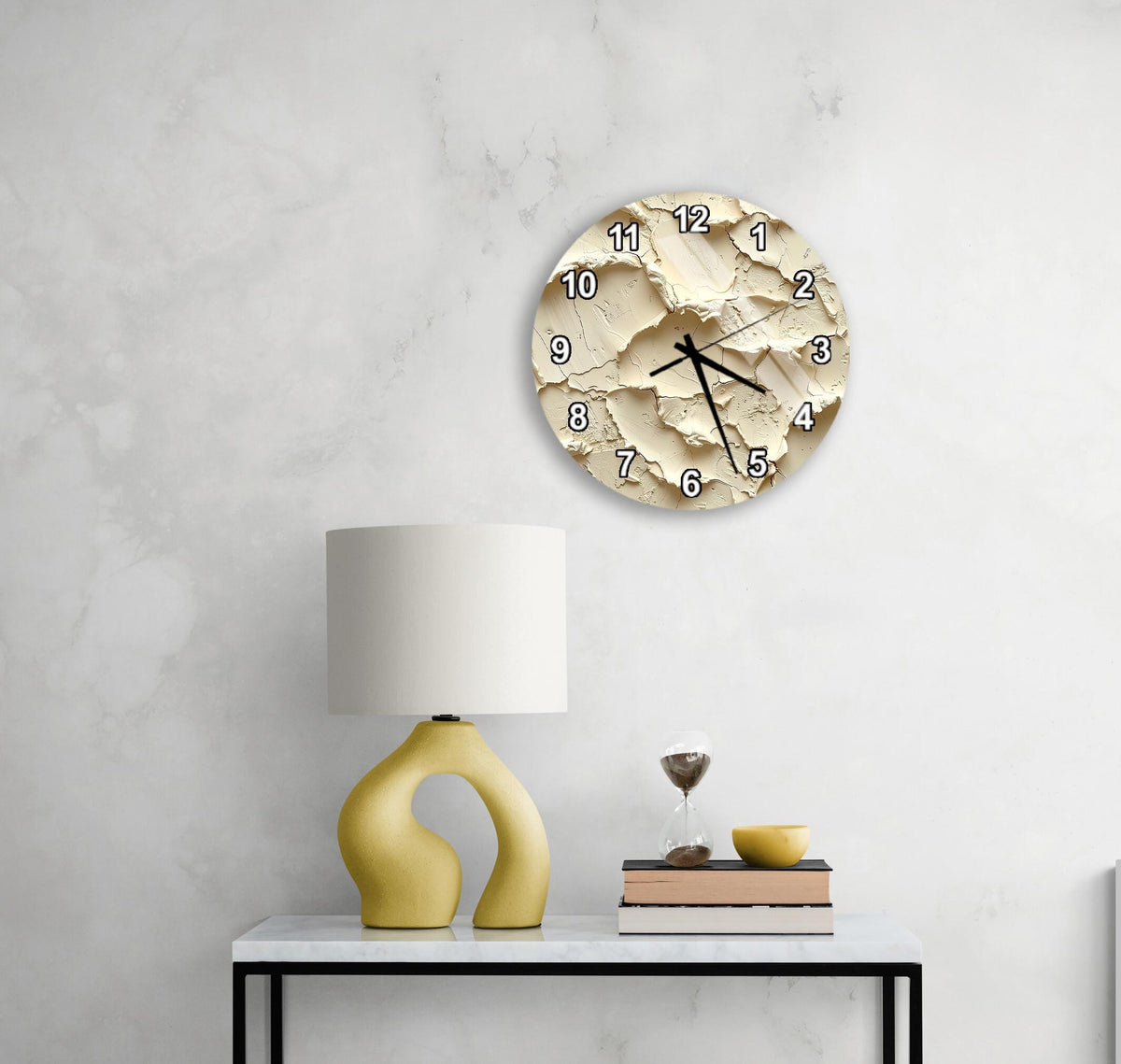 a modern, minimalist living space with a white wall, a round clock with a unique design, a yellow lamp, a stack of books, and a glass of wine on a white table.