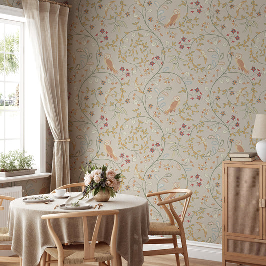 a cozy dining room with a round wooden table set for two, featuring a vase of flowers and a lamp. The walls are adorned with a floral wallpaper pattern, and a window with curtains can be seen on the left side of the room.