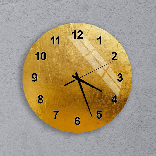 A gold-colored wall clock with black numbers and hands is mounted on a concrete wall.