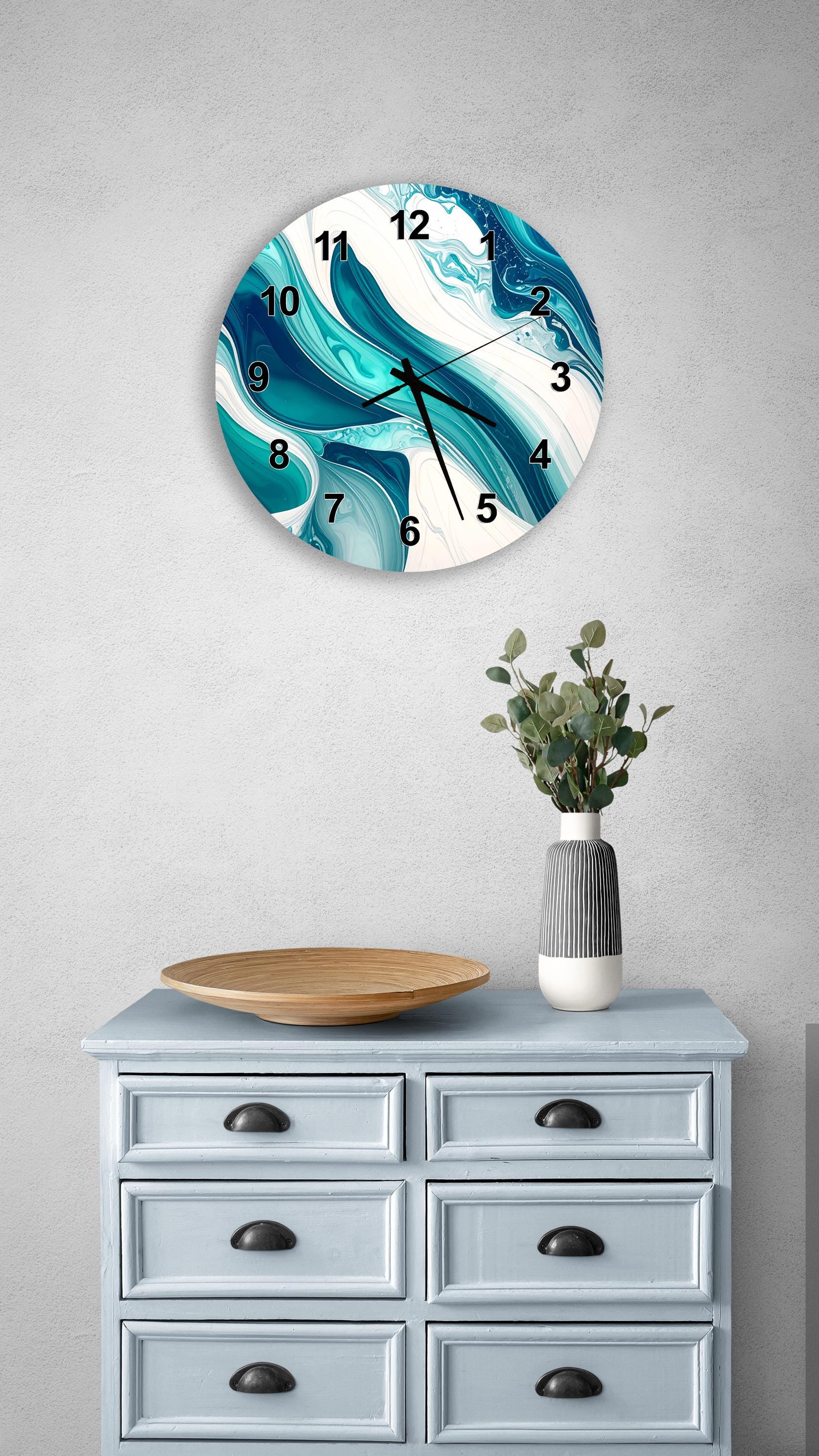 a wall clock with a blue and white abstract design, mounted on a wall above a light blue dresser with six drawers. The dresser also has a vase with greenery and a wooden tray on top.