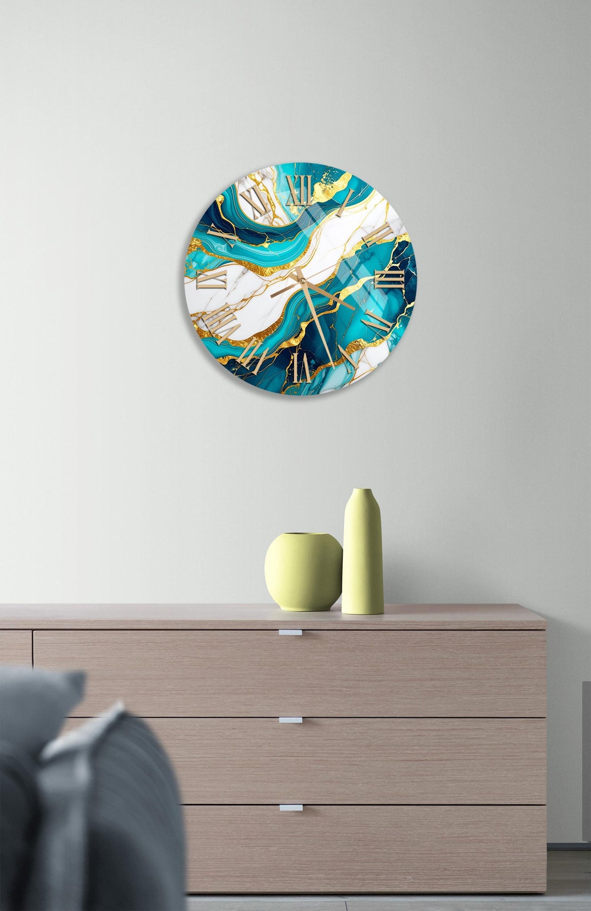 a modern clock with a turquoise and white color scheme, hanging on a wall above a wooden dresser. The dresser has a vase and a small sculpture on top of it.