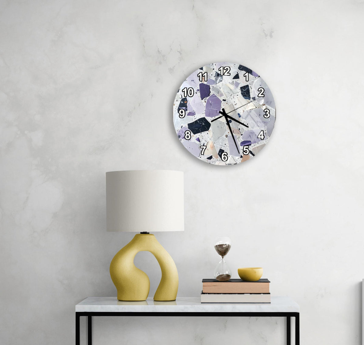 a modern, minimalist living space with a white marble wall, a round clock with a unique design, a yellow lamp with an unusual, curved base, and a small table with a book and a glass of water.