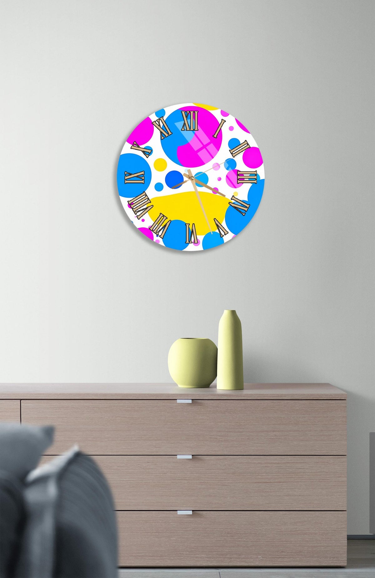 a colorful clock with a unique design hanging on a wall above a wooden dresser.