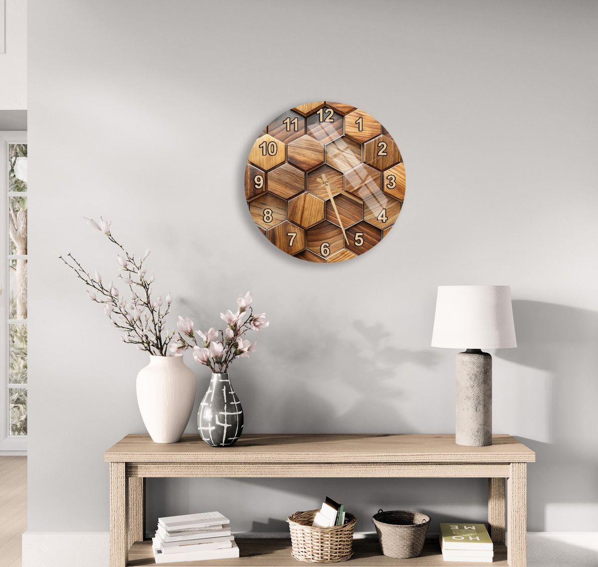 a wooden clock with a hexagonal design, mounted on a wall above a wooden table with various decorative items, including a vase with flowers, a lamp, and a stack of books.