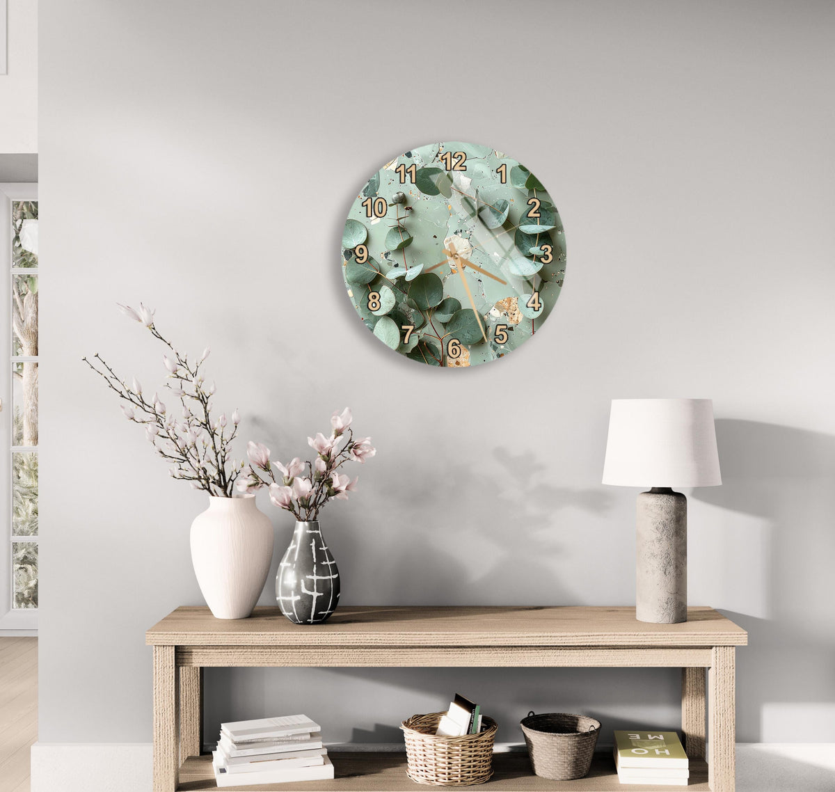 a modern living room with a round wall clock displaying a floral design, a wooden table with a lamp, a vase with pink flowers, and a stack of books.