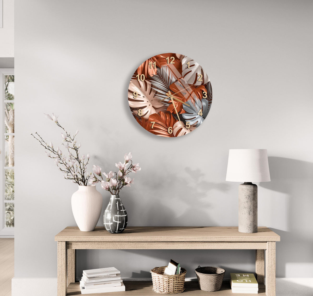 a modern living room with a round wall clock displaying a tropical leaf pattern, a wooden table with a lamp, a vase with flowers, and a stack of books.