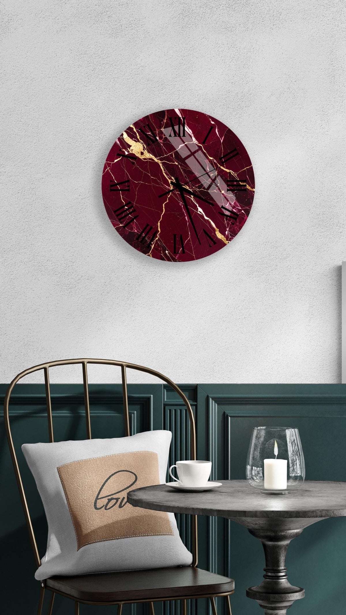 a modern interior design with a maroon and gold marble clock mounted on a white wall above a black metal chair. The chair has a white pillow with the word "love" printed on it. In front of the chair, there is a small table with a glass candle holder and a white teacup.