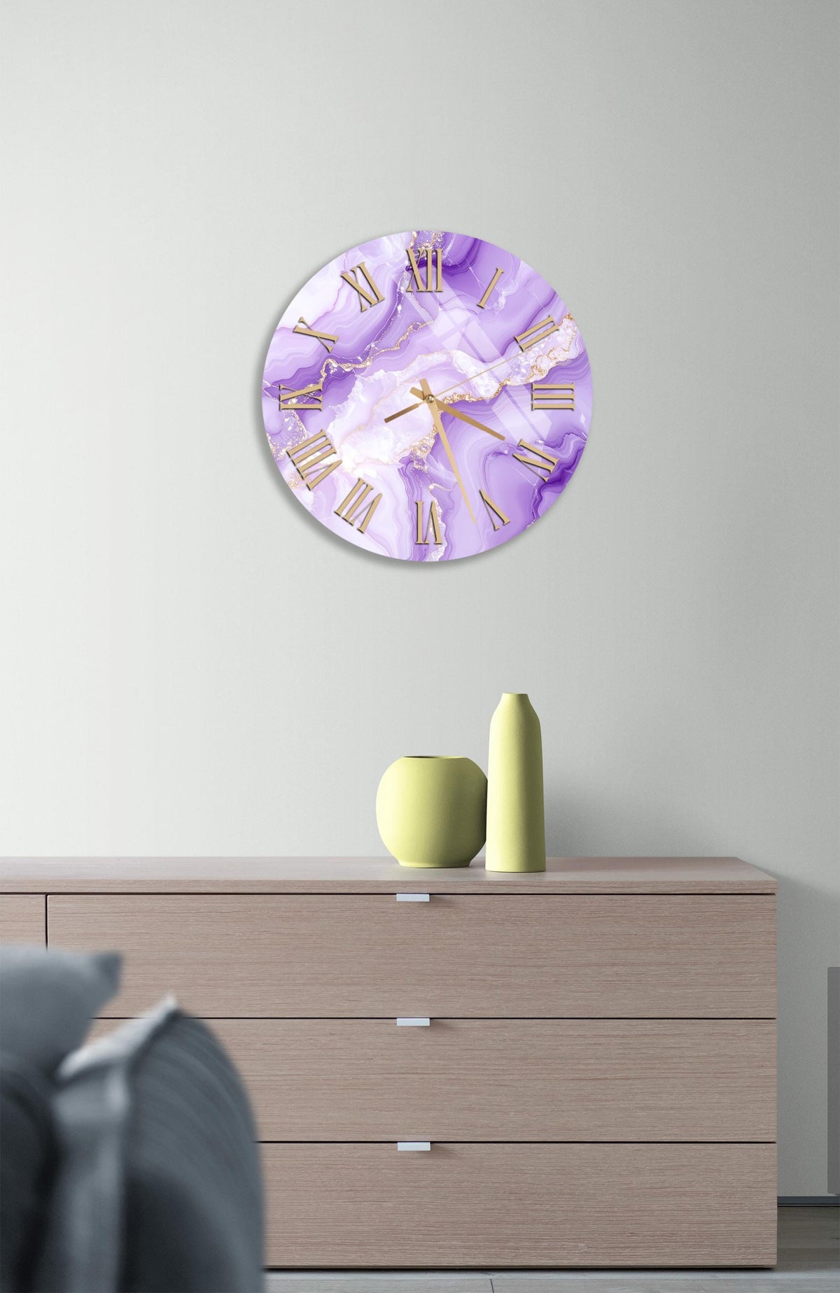 a wall clock with a purple and white marble design, mounted on a wall above a wooden dresser with three drawers.