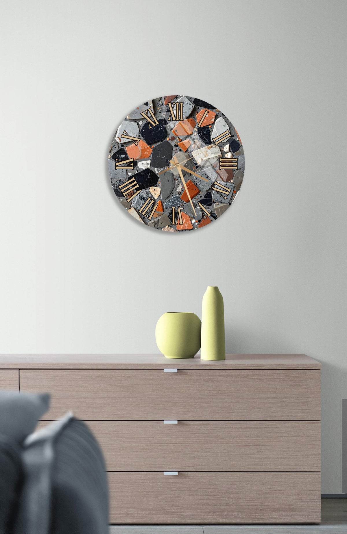 a modern clock with a unique, colorful design hanging on a wall above a wooden dresser. The dresser has three drawers and a vase on top.