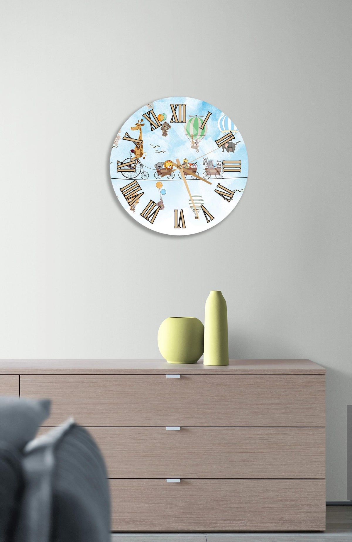 a round clock with a whimsical design, hanging on a wall above a wooden dresser.